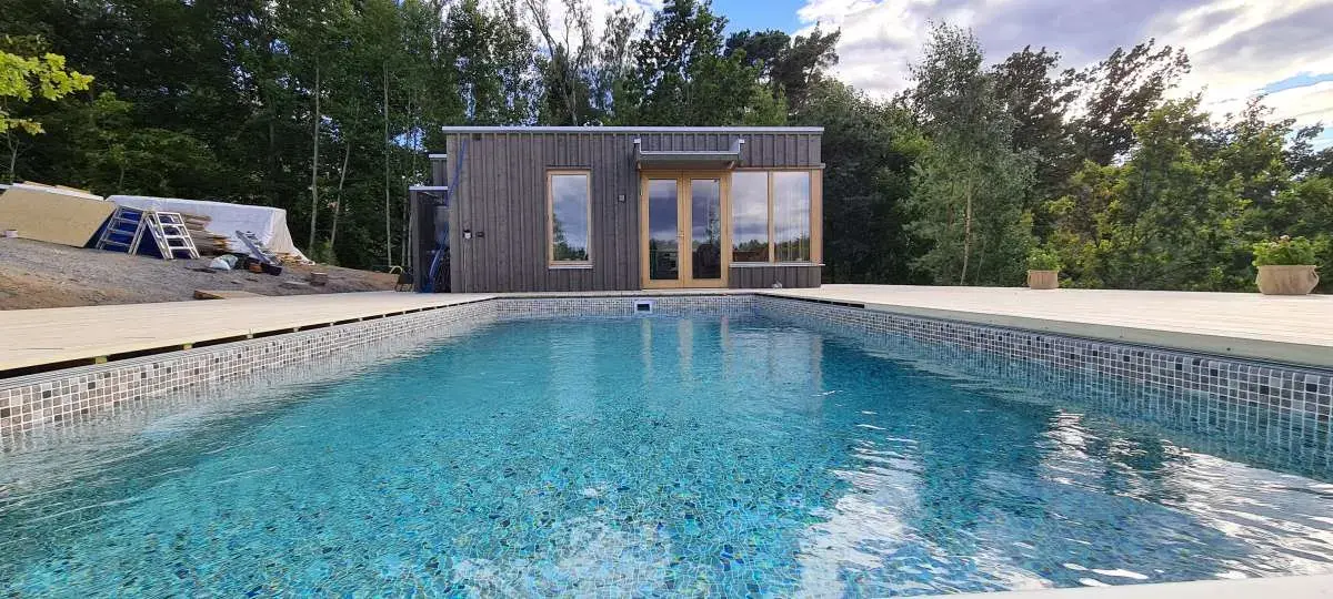 Pool framför det mörka poolhuset på Ingarö